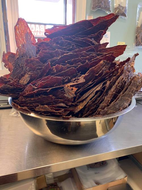 A large bowl filled with stacked, dark brown beef jerky pieces on a countertop.