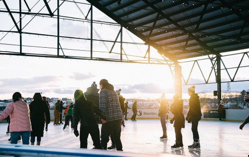 People ice skating under a covered rink at sunset, with a warm glow illuminating the scene.