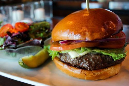 A juicy burger with lettuce, tomato, and onion on a toasted bun, served with a side salad and a pickle.