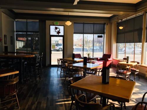 Cozy café interior with wooden tables, chairs, and large windows letting in natural light.
