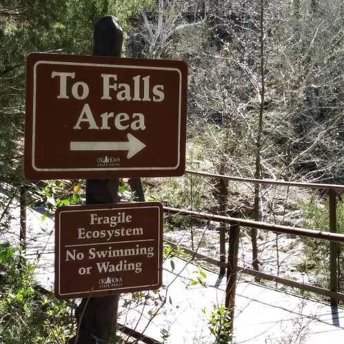 Sign directing to the falls area, with warnings about fragile ecosystems and no swimming or wading allowed.