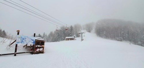 A snowy ski slope with a chairlift, a map sign, and a small building in a foggy winter landscape.