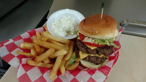 A towering burger with lettuce, tomato, and cheese, served with fries and a side of coleslaw in a red-checkered basket.