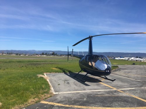 A black helicopter parked on a tarmac with a clear blue sky and mountains in the background.