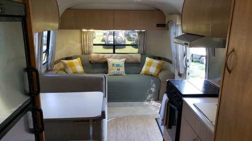 Cozy interior of a camper with a sofa, cushions, kitchenette, and large windows letting in natural light.
