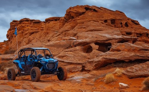 A blue off-road vehicle parked near red rock formations under a cloudy sky.