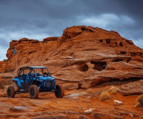 A blue off-road vehicle parked near rugged red rock formations under a cloudy sky.