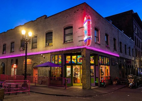 A colorful storefront with neon lights and a vibrant facade, set against a twilight sky.
