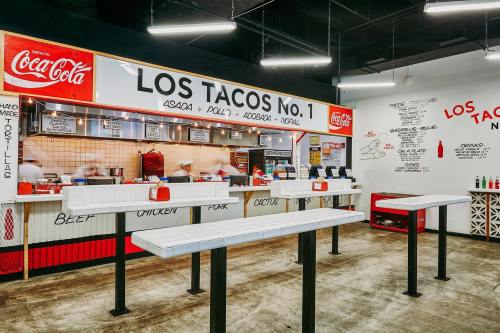 A vibrant taco restaurant interior featuring a counter with menu items and Coca-Cola branding.