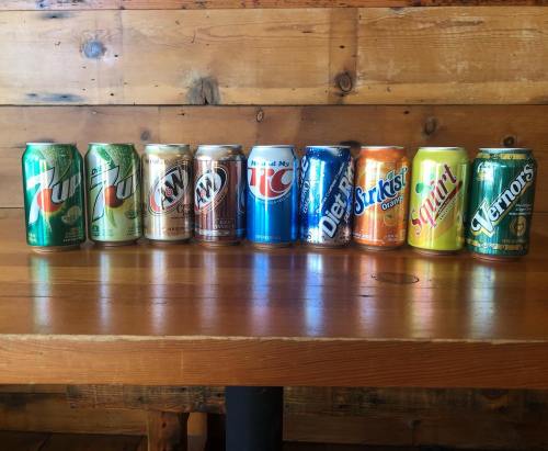 A row of colorful soda cans on a wooden table, featuring various brands and flavors.