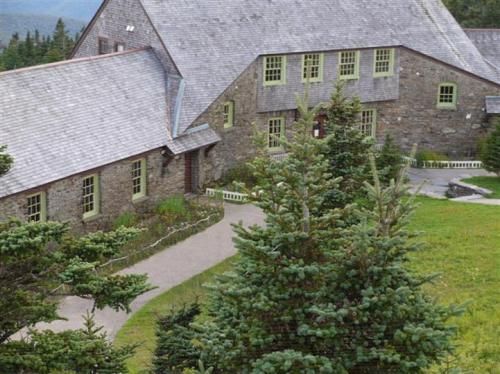 A stone building with green windows surrounded by trees and a pathway, set in a lush, green landscape.