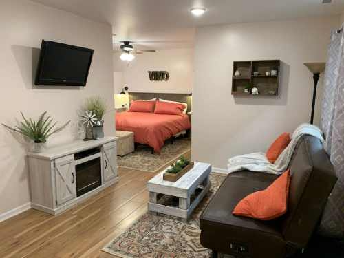 Cozy living area with a brown sofa, TV, and a bedroom with a red bed in a warm, inviting space.