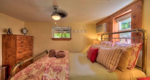 Cozy bedroom with a metal bed, decorative pillows, wooden dresser, and a window with natural light.