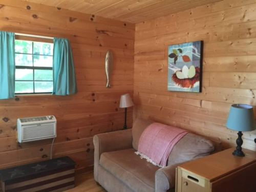Cozy wooden room with a couch, blue curtains, artwork, and an air conditioner.