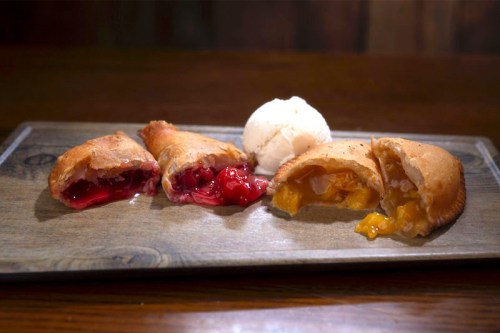 Three fruit-filled pastries on a wooden plate, with cherry and peach fillings, accompanied by a scoop of vanilla ice cream.