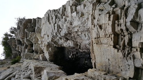 A rugged rock formation with jagged edges and a dark opening, surrounded by sparse vegetation.