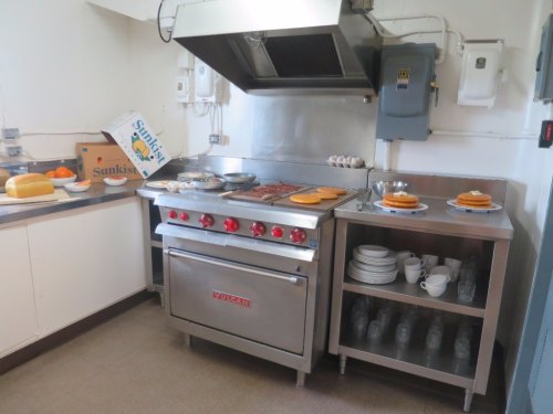 A commercial kitchen with a stainless steel stove, plates of food, and organized shelves of dishes and glasses.