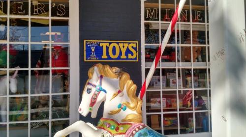 A colorful carousel horse in front of a toy store with a sign that reads "TOYS."