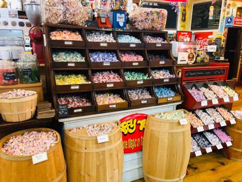 A colorful display of assorted candies in jars and wooden barrels at a candy shop.