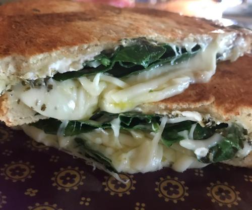 A close-up of a toasted sandwich filled with melted cheese and fresh spinach, showcasing its gooey interior.