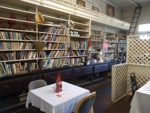 Cozy restaurant interior with white tables, a bookshelf filled with books, and decorative items on display.