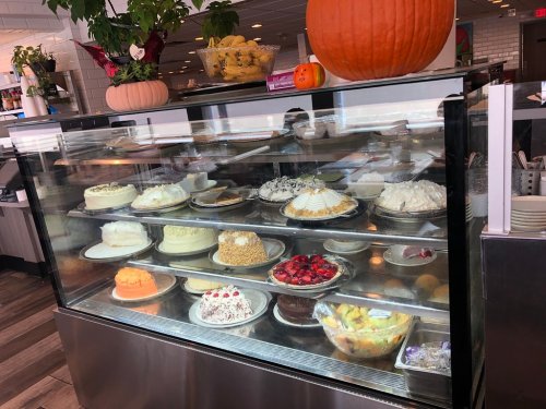A display case filled with various cakes and desserts, including fruit, cream, and chocolate options, in a cozy restaurant.