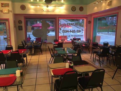 A cozy diner interior with empty tables, colorful tablecloths, and large windows showing an outdoor patio.