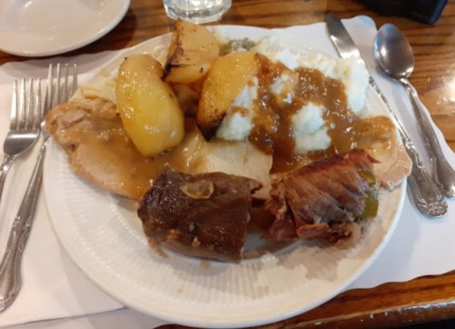A plate of food featuring sliced turkey, mashed potatoes with gravy, baked apples, and a piece of ham.
