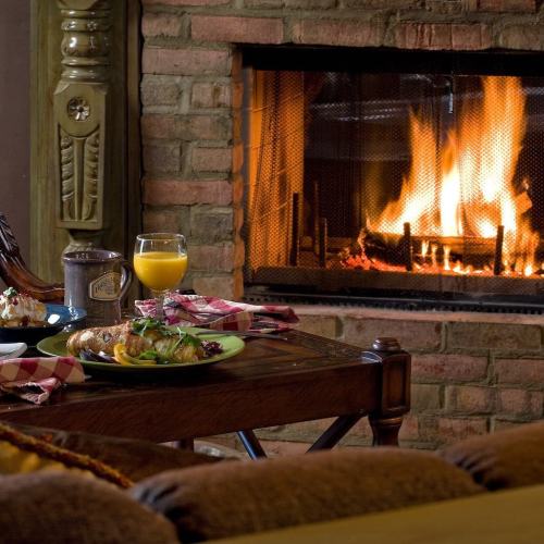 A cozy scene with a fireplace, a wooden table set with a meal, and a glass of orange juice. Warm and inviting atmosphere.