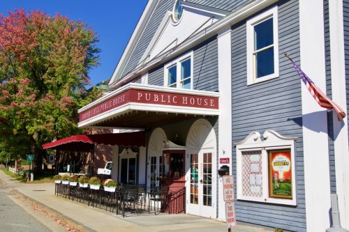 A charming public house with a red awning, surrounded by trees and a clear blue sky. American flag displayed.