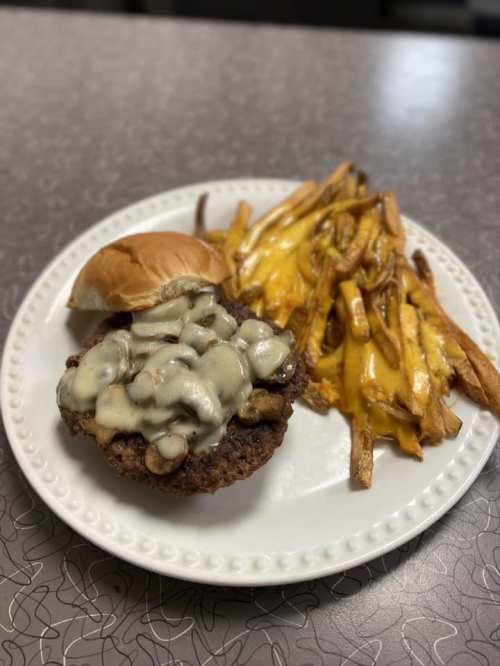A plate with a cheeseburger topped with mushrooms and a side of cheesy fries.