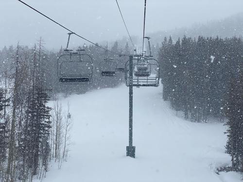 A snowy ski resort scene with a chairlift and trees, surrounded by falling snowflakes.