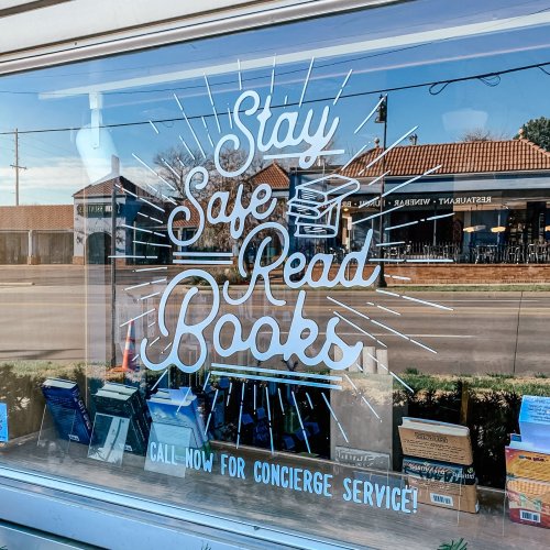 Window display with the text "Stay Safe Read Books" and a call for concierge service, featuring books in the foreground.