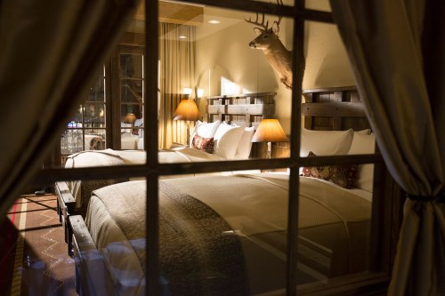 Cozy hotel room with two beds, warm lighting, and rustic decor, viewed through a window with curtains.