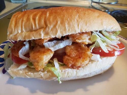 A sandwich filled with crispy fried shrimp, lettuce, and tomato, served in a soft bun on a plate.