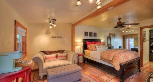 Cozy bedroom with a bed, sofa, and decorative accents, featuring warm colors and natural light.