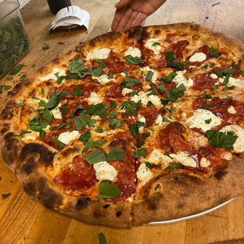 A freshly baked pizza topped with pepperoni, dollops of ricotta, and fresh basil on a wooden surface.