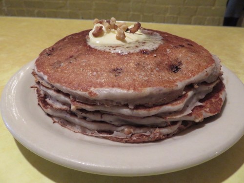 A stack of fluffy pancakes topped with a dollop of butter and a walnut, served on a white plate.