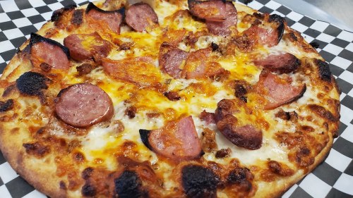 A close-up of a pizza topped with melted cheese, pepperoni, and crispy edges on a checkered paper background.