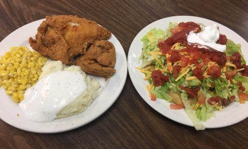 A plate with fried chicken, mashed potatoes with gravy, corn, and a salad topped with cheese, salsa, and sour cream.