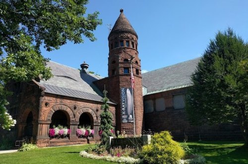 Historic building with a tall tower, surrounded by greenery and flowers, under a clear blue sky.