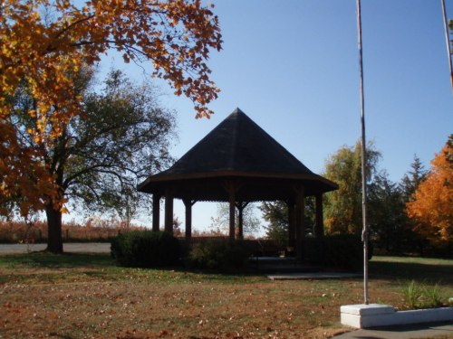 A wooden gazebo surrounded by colorful autumn trees under a clear blue sky.