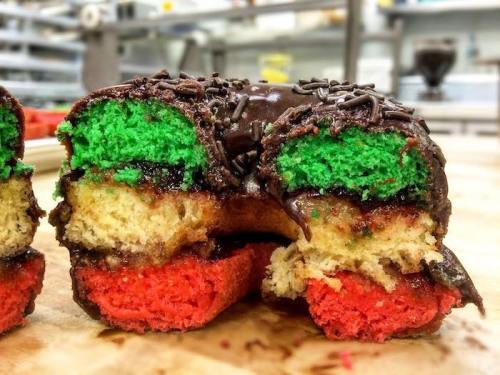 A cross-section of a colorful donut with green, yellow, and red layers, topped with chocolate and sprinkles.