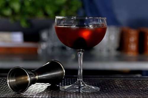 A cocktail in a coupe glass sits on a bar, with a jigger lying beside it.