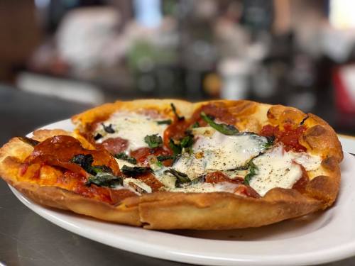A freshly baked pizza topped with pepperoni, mozzarella, and fresh basil on a white plate.