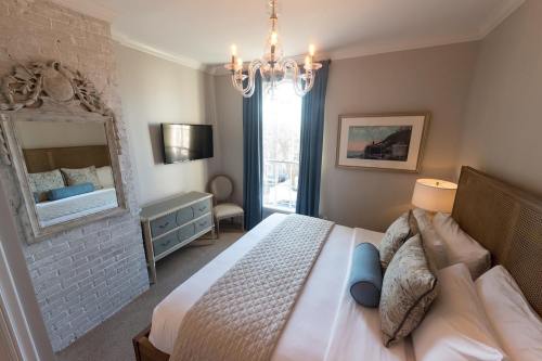 Cozy bedroom with a chandelier, large mirror, TV, and a neatly made bed, featuring soft colors and natural light.