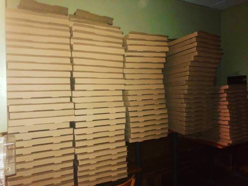 A large stack of empty cardboard boxes neatly arranged against a wall in a dimly lit room.