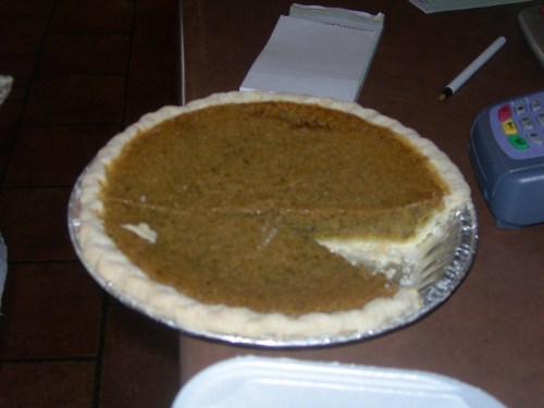 A partially sliced pumpkin pie in a silver pie dish on a countertop.