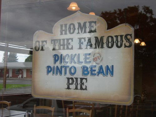Sign in a window reading "Home of the Famous Pickle or Pinto Bean Pie" with a decorative border.