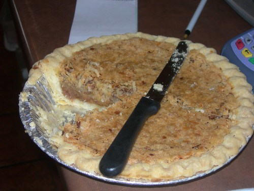 A partially sliced pie in a silver tin, with a black knife resting on the crust.